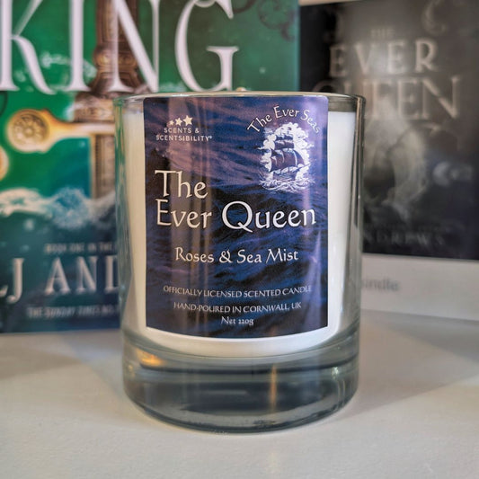 Candle labeled 'The Ever Queen: Roses & Sea Mist' with a blurred book in the background