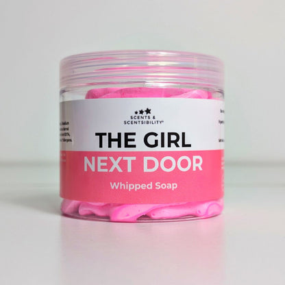Jar of pink whipped soap labeled 'The Girl Next Door' on a light gray background