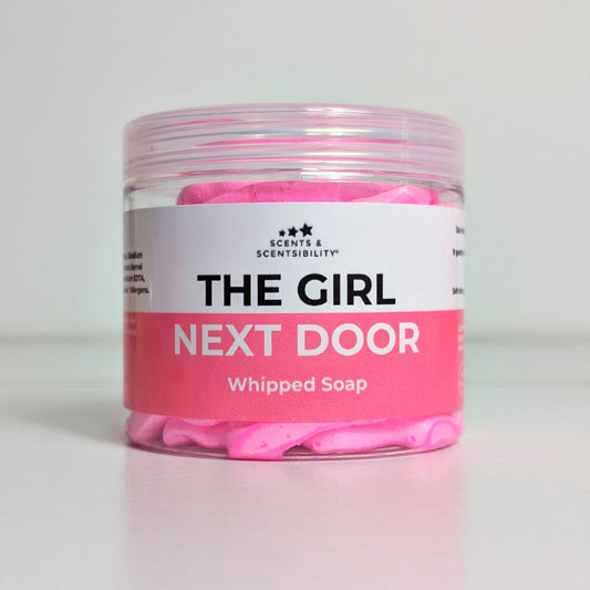 Jar of pink whipped soap labeled 'The Girl Next Door' on a light gray background