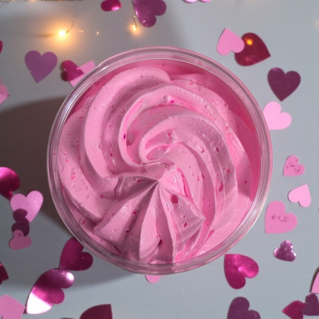 Pink whipped soap in a container with heart-shaped confetti on a light grey background