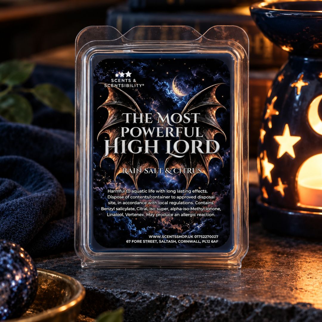 A wax melt package labeled 'The Most Powerful High Lord' by Scents & Scentsibility, shown in a clear clamshell container on a dark tabletop with warm ambient lighting and decorative lanterns in the background.