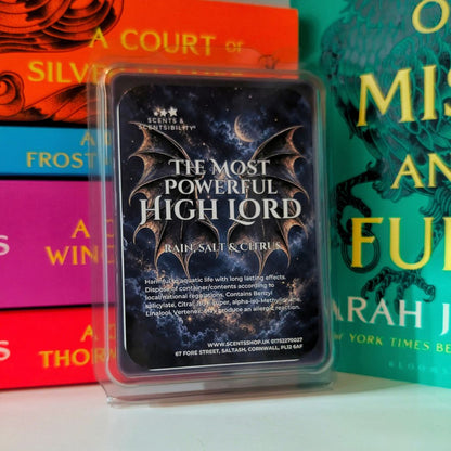 A packaged wax melt, labeled "The Most Powerful High Lord" by Scents & Scentsibility, photographed in front of colorful ACOTAR books. 