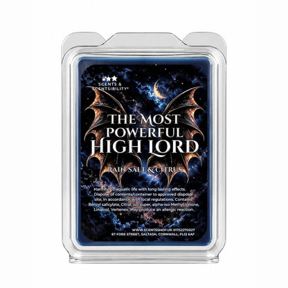 A clear plastic clamshell wax melt container on a white background, showing a dark blue label with a cosmic wings design and the text 'THE MOST POWERFUL HIGH LORD' and 'RAINS, SALT & CITRUS'.