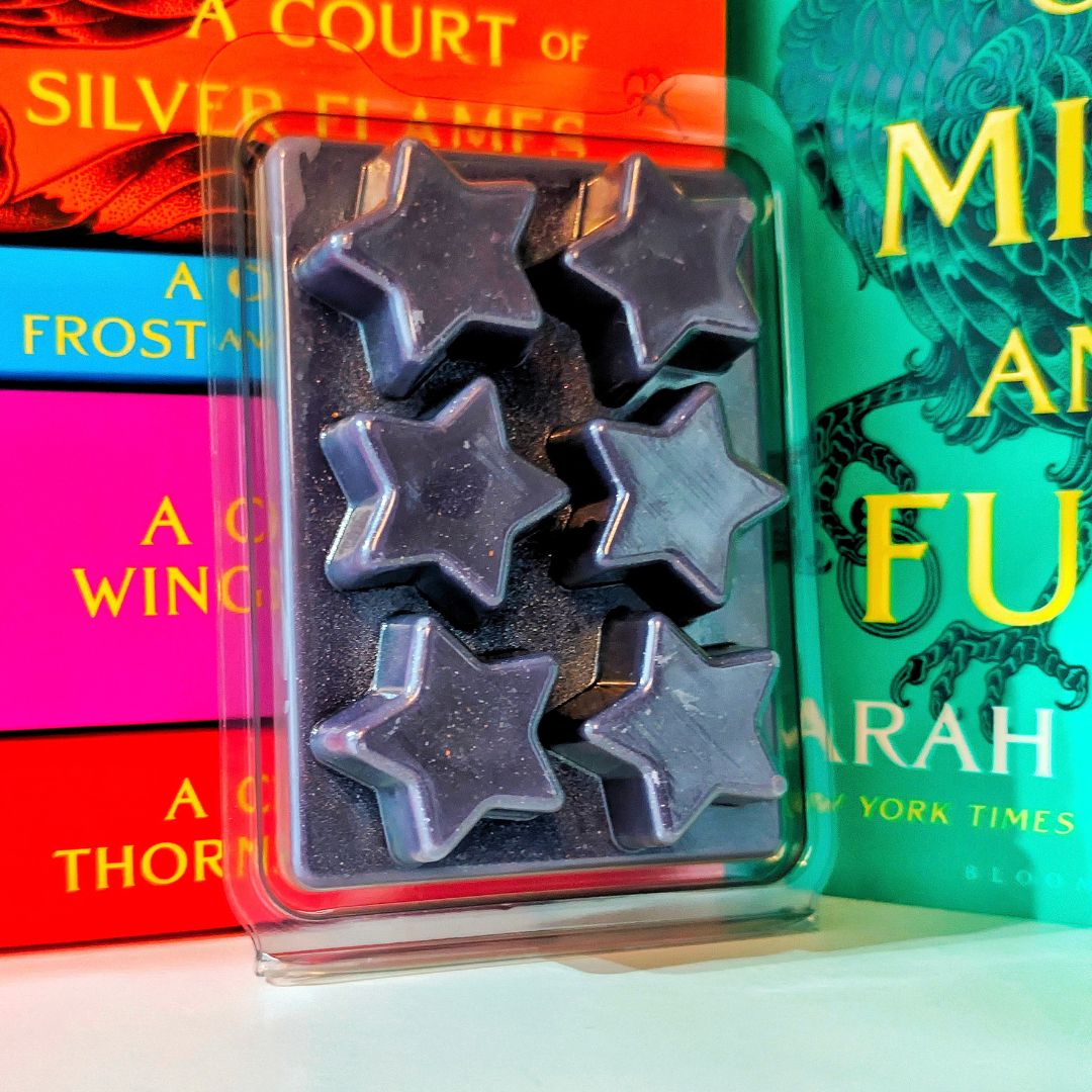 Six star-shaped wax melts in a clear plastic clamshell package, displayed in front of colorful book spines.