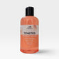 A bottle of Scents & Scentsibility 'Toasted Marshmallow' 4-in-1 liquid soap, featuring a translucent peach-colored liquid inside a clear bottle with a black cap, set against a light gray background.