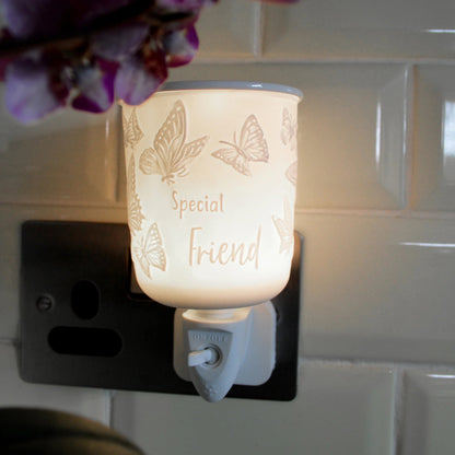 A butterfly-themed plug in wax melt warmer labeled 'Special Friend' glowing with a warm light, plugged into a black wall outlet against a white tiled wall.