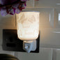 A butterfly-themed plug in wax melt warmer labeled 'Special Friend' glowing with a warm light, plugged into a black wall outlet against a white tiled wall.