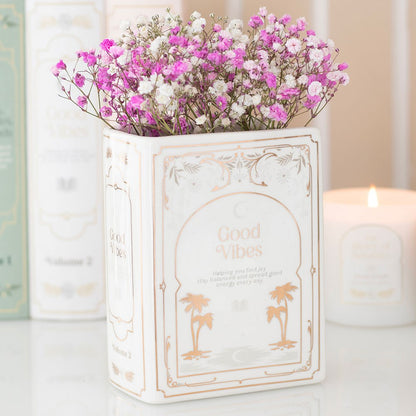 Decorative vase with 'Good Vibes' text and pink flowers on a light background