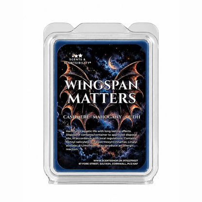 A clear plastic clamshell package containing a blue scented melt bar labeled 'Wingspan Matters' with fantasy dragon artwork and text reading 'Cashmere - Mahogany - oudh'.