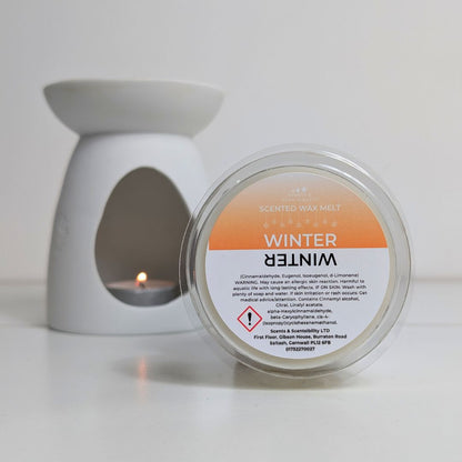 Scented wax melt container labeled 'Winter' with a lit candle in the background.
