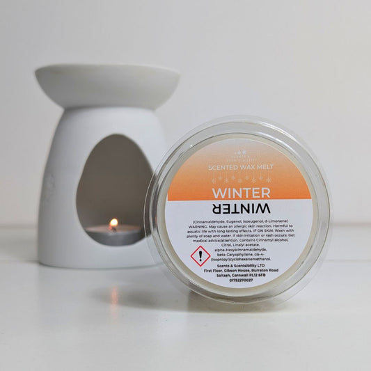Scented wax melt container labeled 'Winter' with a lit candle in the background.