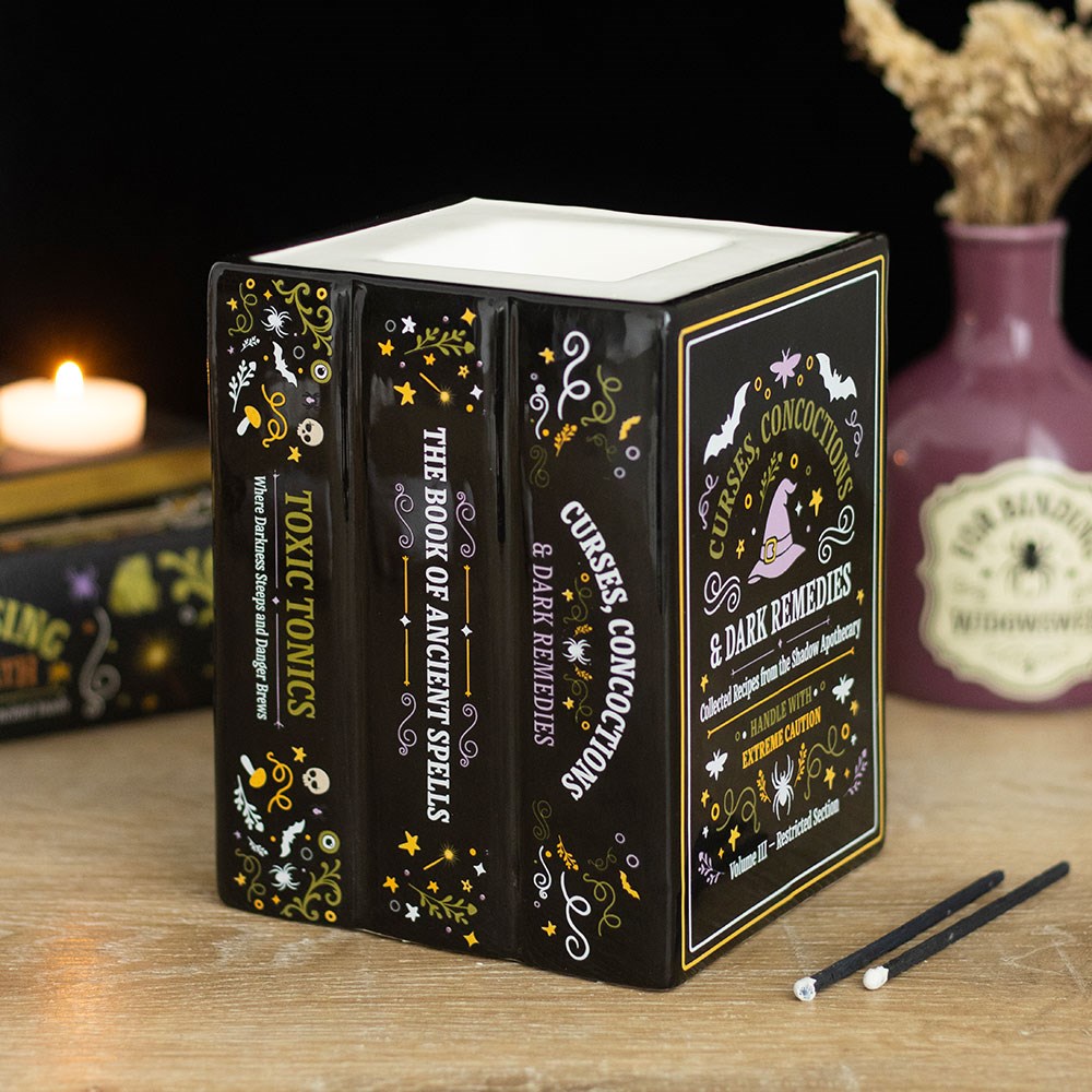 A black, decorative wax melt and oil burner, shaped like a stack of books about ancient spells and curses