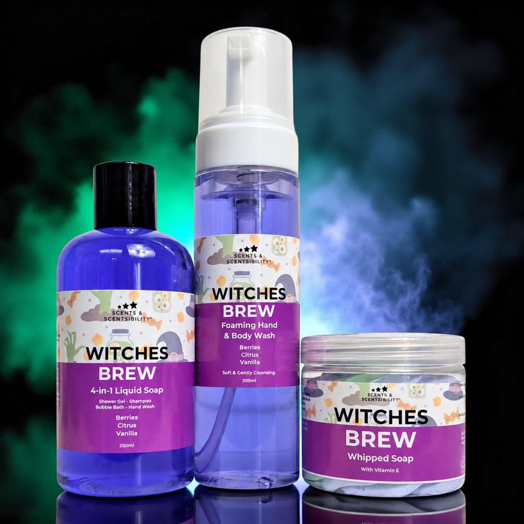 Three Witches Brew branded personal care products displayed together: a blue bottle of 4-in-1 liquid soap, a tall clear bottle with a white pump of foaming hand & body wash, and a clear jar of whipped soap, all with purple labels, set against a dark smoky background with green and blue glow.