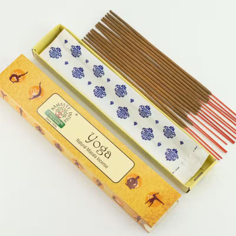 A box of Namaste Yoga incense sticks shown open on a white background, with several brown incense sticks and red tips visible inside the box. The box is yellow with blue floral patterns and a front label reading 'Namaste Yoga' and 'Yoga Natural Incense Sticks'.